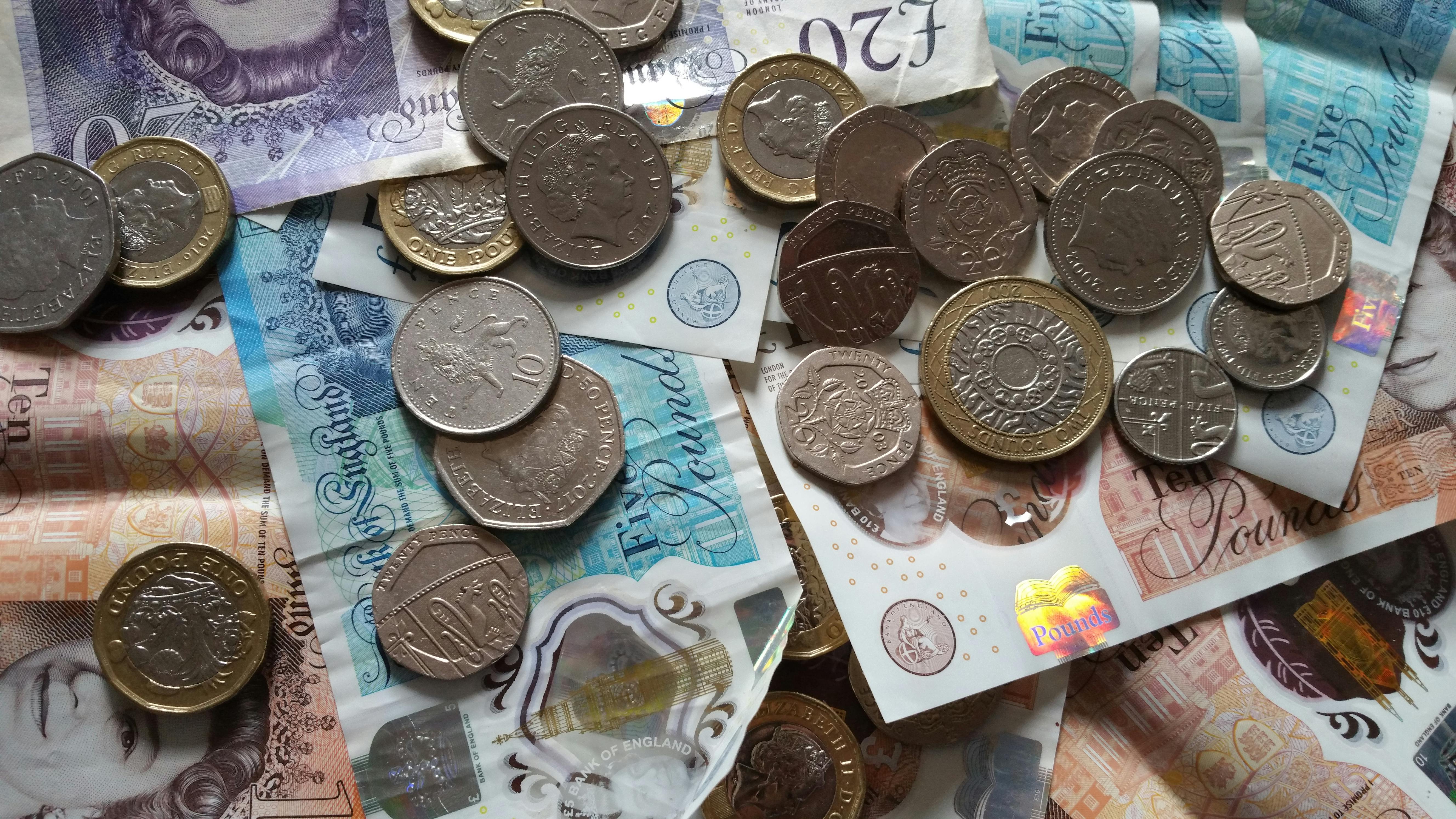 A scattered pile of British currency, including various coins and banknotes of different denominations such as £5, £10, £20 notes, and £1, 50p, 20p, and 10p coin